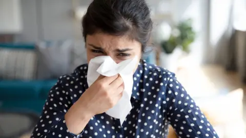 Getty Images A woman at home holds a tissue to her face as she struggles with a cold