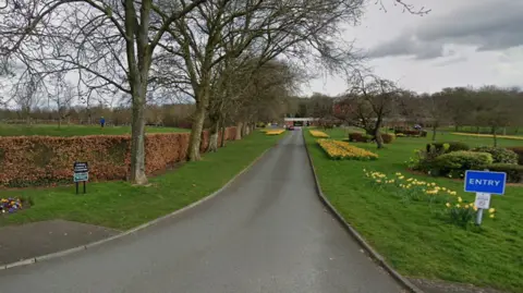 Google A Google Street View image of the road leading into St Helens crematorium. The road is lined on both sides by turf and flower beds.