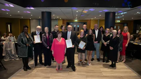 City of Wolverhampton Council A group of people at an awards evening in a function room, dressed smartly and holding certificates.