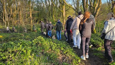 Lauren Murphy A group of people walking through a grassy woodland area. It appears to be sunset.