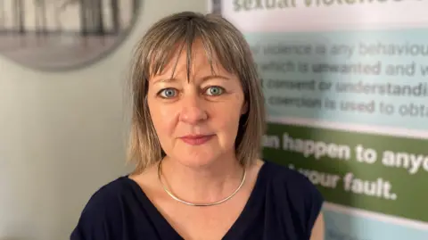A woman with bobbed grey hair and a fringe, a black top and silver necklace. 