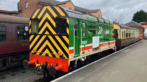 BBC A locomotive is painted yellow and black at the front and mainly green down the side. The photo is taken from the platform and the side includes the words Vanguard, Severn Valley Railway and powered by hydrogen.
