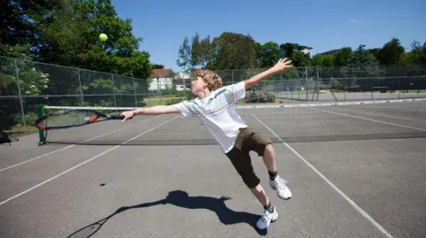 Stock photo of a buy stretching to reach a tennis ball. He is on a tennis court and his shadow can be seen in the picture. 