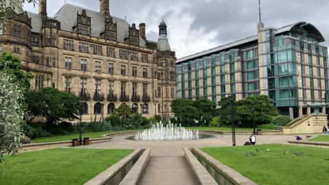 A water feature surrounded by neatly mown grass and a large old building