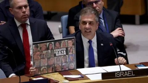 Reuters Israeli Foreign Minister Eli Cohen holds up a poster showing kidnapped Israeli children during a speech at the UN Security Council in New York (24 October 2023)