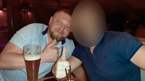 VK Two men with large glasses in front of them giving a thumbs up sign to the camera. The one on the left, Ruslan Yeriomichev, has a trimmed beard and close-cropped hair, and is wearing a light patterned T-shirt. The face of the man on the right has been blurred. 