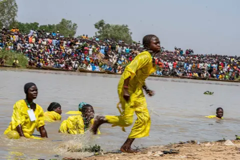 Sani Maikatanga Girls in yellow uniforms emerge from the water after having tried to catch some fish.
