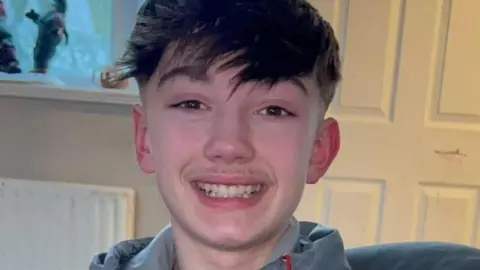 Christopher McBurnie, a teenager with short dark hair and a long fringe, smiling.