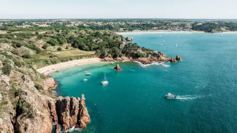 Overhead shot of the coastline with a few boats in clear blue waters and white sandy beaches