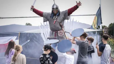 A man dressed as a knight with children holding shields. The children are not in view.
