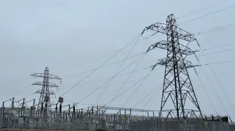 Spittal substation, Caithness - Two large electricity pylons and multiple power lines rise above a fenced electrical substation under an overcast sky.