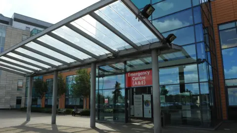 The Peterborough hospital emergency department building - with a glass frontage and glass door and a red emergency sign board.