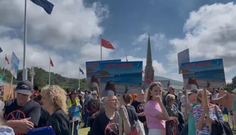 A group of people holding Picketts saying 'Not4IoM' protest against a new windwarm being build. 
