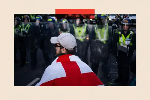 SOPA Images/LightRocket via Getty Images A man drapped in an England flag stands in front of police lines as clashes erupt in Southampton 