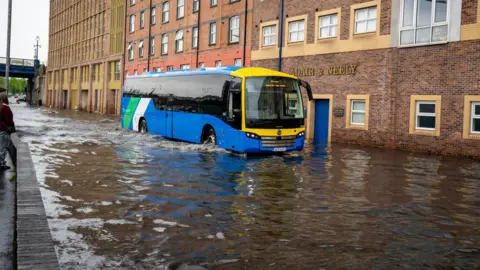 A bus drives through a heavily flooded street