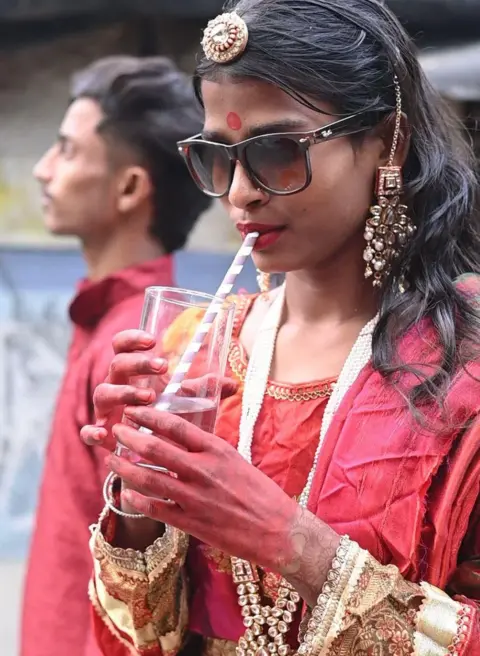 Innovation for Change A girl wearing colorful red clothes, jewelry and sunglasses drinks from a glass through a straw at the much-talked-about fashion show.