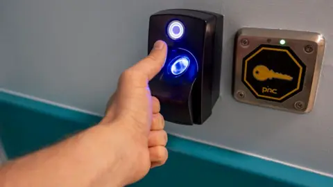 Close up of a person's left hand about to place their thumb on the scanner, which is glowing blue