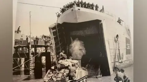 William Wake A black and white image of a tank leaving a ship during the D-Day landings. You can see men standing at the top watching the tanks come off.