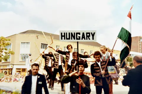 Walter Crinnion A group of men in black jackets and shirts with gold tassels holding a sign with the word Hungary on it and the flag of that country.