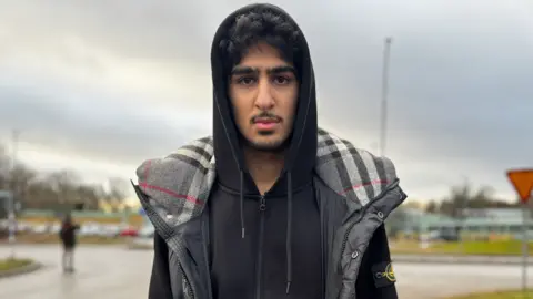 BBC Man with moustache wears black sweatshirt and grey puffy vest while facing camera