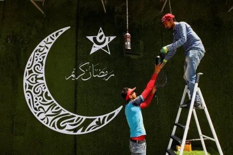 Reuters A worker stands on a ladder and hangs a fanous lantern