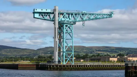 A large crane on the banks of a river. It is painted turquoise/blue. 