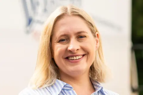 Dunsters Farm Hanna Barlow with shoulder length blonde hair wearing a blue and white striped shirt and smiling at the camera