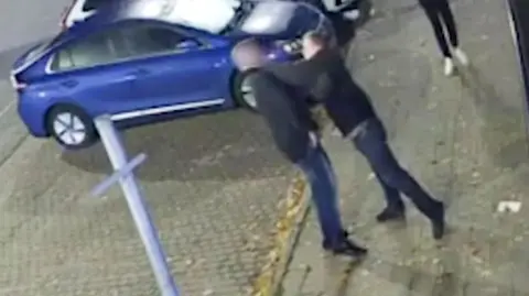 South West News Service A grab from footage obtained by the Daily Mail purporting to show Mike Amesbury in a street altercation, in shot is one man appearing to punch another, on a street with a blue car in the background.