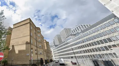 General view of Abbey Orchard Street showing cars on the road, a brown brick building to one side and a large office block to the other.