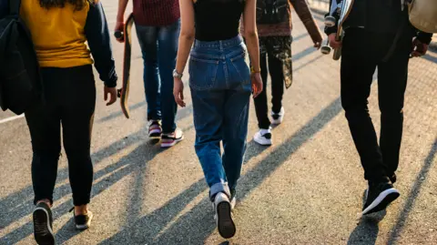 Rear view of a group of school friends walking outdoors dressed in  jeans and trainers