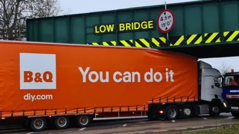 Damian Tarnowski  B&Q lorry bearing a logo that says 'you can do it' stuck under a bridge