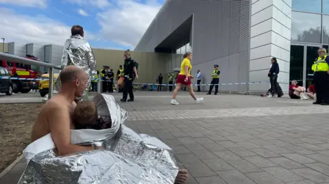A man and child draped in a foil sheet outside the leisure centre