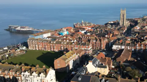 Martin Barber/BBC An aerial image of Cromer showing town centre buildings and houses, a medieval church and tower, the pier and sea.