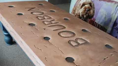 A table painted to look like a giant bourbon biscuit. A cushion with the image of a dog is in the back.