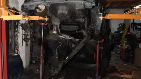HSE The inside of a garage showing a black cad suspended at its back end on a red metal column, while its front is resting on the ground