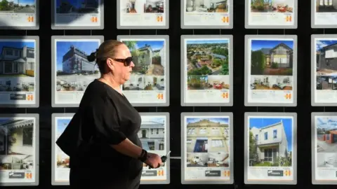 Getty Images Woman walking by estate agent window