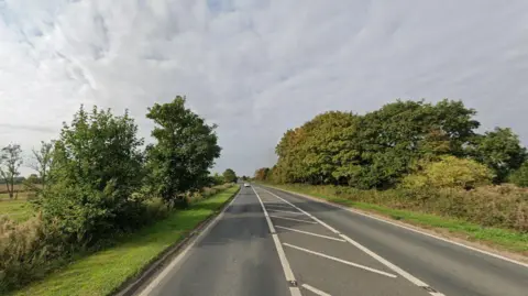 Google road view of B1230 near Gilberdyke heading towards Howden. There are trees each side of the road and a long stretch of road ahead. Only one car can be seen in the distance.