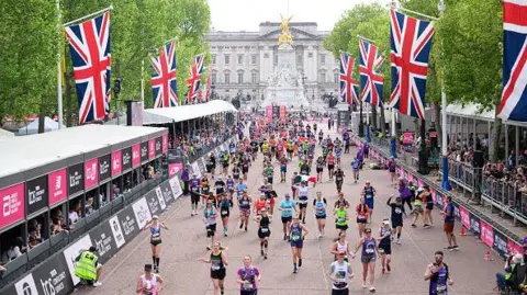Runners approach the finish area on The Mall, with Union flags lining the route and Buckingham Palace visible in the background.