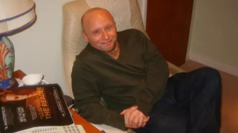 Handout Dan Kay smiles at the camera while sitting in a leather armchair. He is bald and is wearing a green sweatshirt and jeans