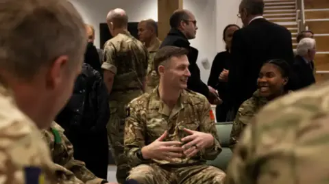 Ministry of Defence Crown Copyright Individuals chatting, at the centre of the image is a man and a women. They are both wearing camouflage Army uniform. 