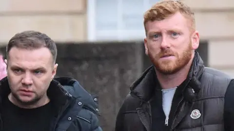 Spindrift Eddie Lyons, left, who has short, dark hair and is looking slightly off camera. He is wearing a dark jacket over a dark t-shirt. Ross Monaghan, right, is looking straight at the camera. He has ginger hair and a ginger beard and is wearing a dark gilet over another dark top.