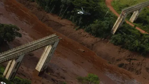 Getty Images A helicopter flies over a dam owned by Brazilian miner Vale SA that burst, in Brumadinho, Brazil