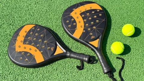 Getty Images Black and orange padel rackets on green court surface with two yellow tennis balls