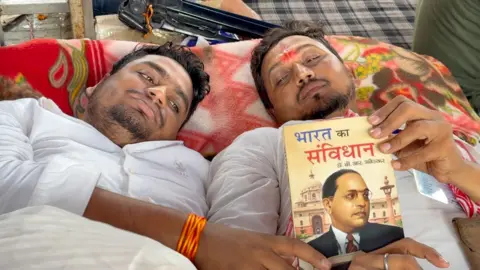 Sartaj Alam Two protesters on a hunger strike seen laying down at the protest site. They are holding a copy of the Indian constitution. 