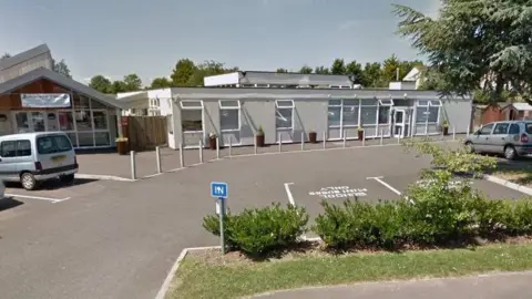 Google Selworthy Special School in Taunton seen from the outside in a screen grab from Google street view. It is a one-storey building with a grey exterior and there is a car park next to the main entrance