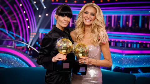 BBC/Guy Levy Claudia Winkleman and Tess Daly smiling while holding miniature glitterball trophies