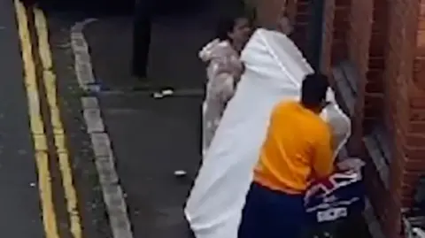 A man and a woman leaving a mattress against a brick wall