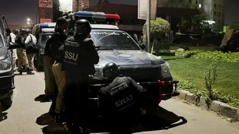 Police officers take position after a police office building was attacked by gunmen in Karachi 17 February