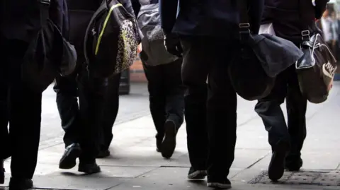 Five pupils, seen from the back, are carrying a bag.