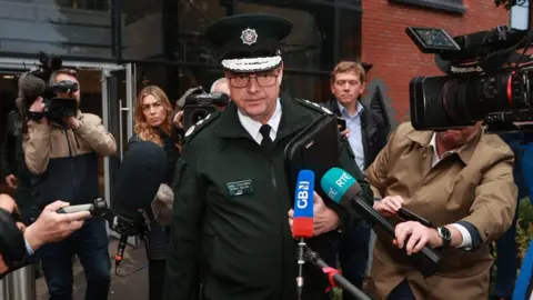 PA Media Simon Byrne walks past journalists, TV cameras and microphones days before his resignation as PSNI chief constable